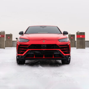 Red Lamborghini Urus on snowy rooftop parking.