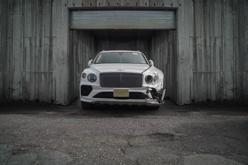A white luxury SUV with front-end damage parked in an urban setting.