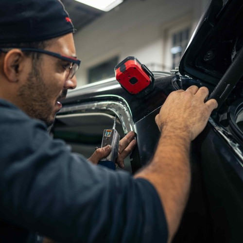 Mechanic inspecting car engine with a diagnostic tool in a workshop.
