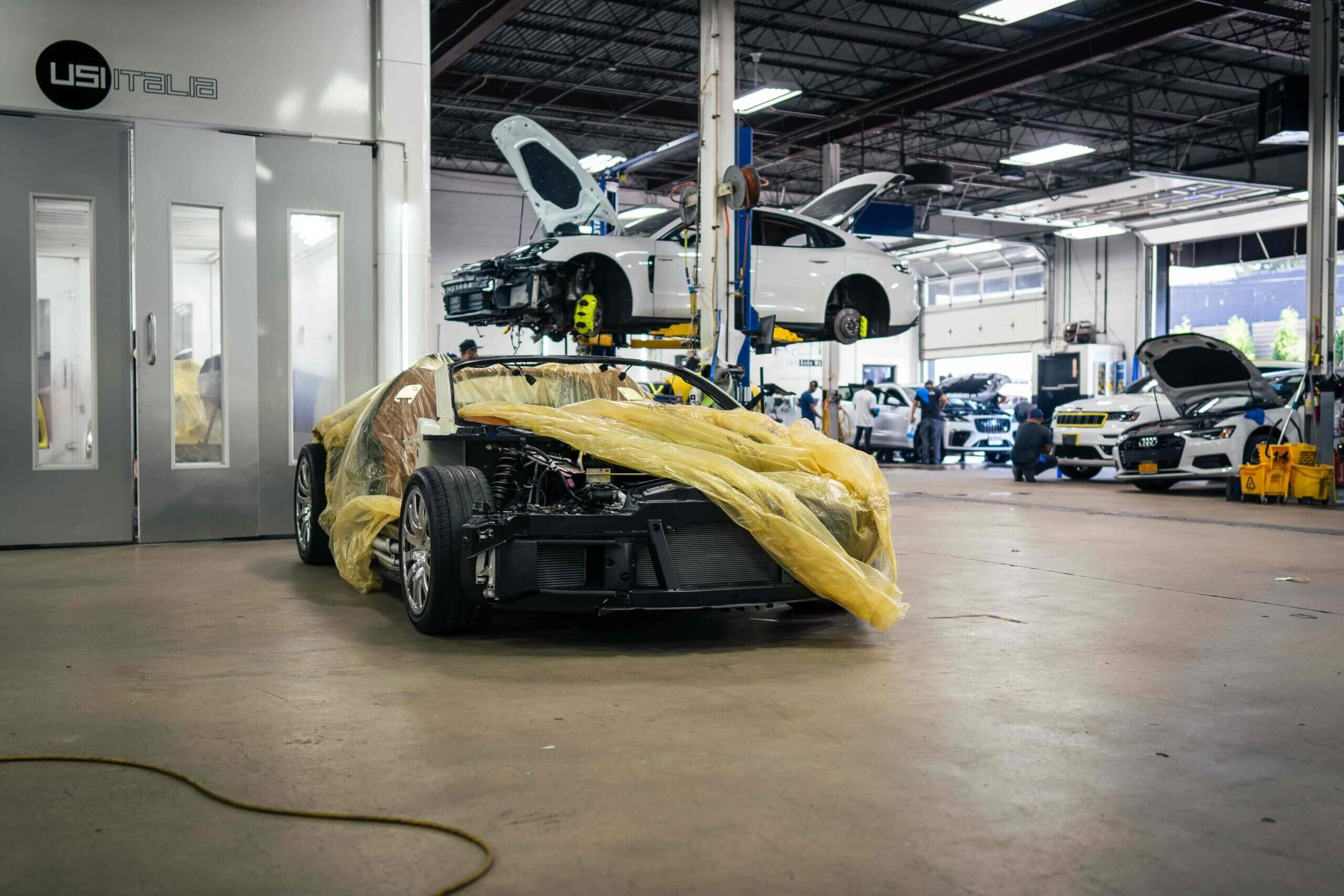 A car covered with a yellow tarp in a repair shop.